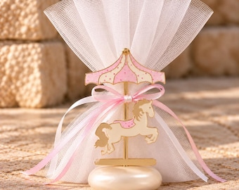 May include: A carousel-themed favor featuring a cream-colored horse and a pink and white striped canopy top. The ornament stands on a smooth, round, off-white base and is wrapped in a fan-shaped white tulle fabric tied with a pink ribbon.