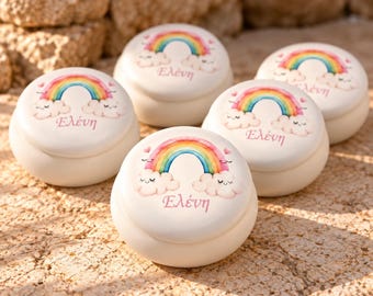May include: Five round white ceramic trinket boxes, each featuring a colorful rainbow graphic with smiling clouds and the Greek name "Ελένη" printed in pink script on the lid. The containers have a smooth, matte finish.