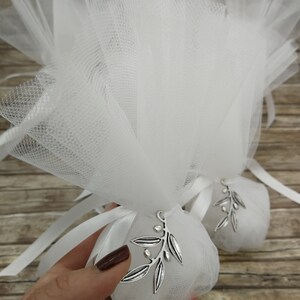 May include: White tulle favor bags with silver olive branch charms. The bags are tied with white satin ribbon.