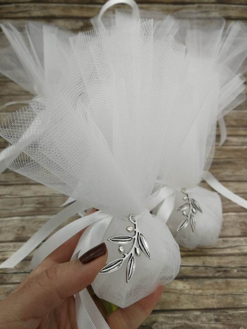 May include: White tulle favor bags with silver olive branch charms. The bags are tied with white satin ribbon.