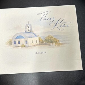 May include: A square invitation featuring a watercolour illustration of a Greek Orthodox church with a blue dome and bell tower. The names "Pavlos & Katia" are written in cursive script, and the date "11.07.2026" is below the image.