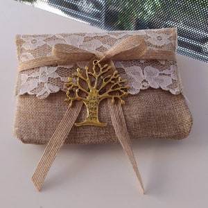 May include: A small, brown burlap pouch with a white lace trim and a gold tree-shaped charm. The charm has the words "Giaite Agouri You You Tuxn Sigti" inscribed on it.
