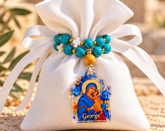 May include: A white fabric drawstring pouch featuring a beaded bracelet with turquoise spheres, small white cross beads, and gold accents. A clear acrylic pendant displays a colorful religious icon of a mother and child with the name George.