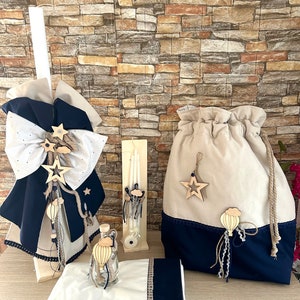 May include: A baptism set featuring a white and blue towel, a white candle, a white and blue bag, a clear glass bottle with a hot air balloon charm, and a white and blue christening gown with a star and hot air balloon charm.