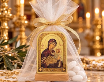 May include: A rectangular religious icon featuring a depiction of the Virgin Mary and Child, set on a light wooden base. The icon is enclosed in a white tulle drawstring bag tied with a gold ribbon, accompanied by several white almond candies.
