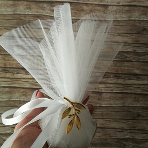 May include: White tulle favor bag with a gold olive branch design. The bag is tied with a white satin ribbon.