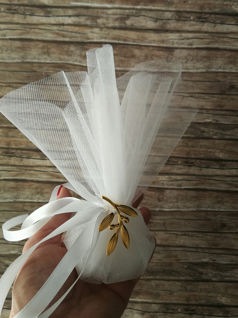May include: White tulle favor bag with a gold olive branch design. The bag is tied with a white satin ribbon.