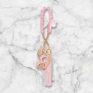 Pode incluir: Encanto de carro de contas cor-de-rosa com um pingente de borboleta dourado e uma borla rosa.