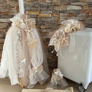 May include: A white suitcase with a decorative seashell and starfish embellishment.  The suitcase is decorated with white and beige tulle and lace.  There is a matching candle with a white candle and a white and beige tulle and lace decoration.  The candle is on a wooden stand with two additional white candles.