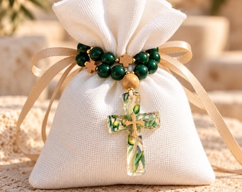 May include: A white fabric drawstring pouch tied with a beige ribbon, adorned with a strand of dark green beads and small wooden crosses. A clear resin cross pendant containing embedded olive branch illustrations hangs from the center.