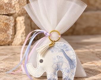 May include: A white tulle favor bag tied with pastel ribbons and a gold keyring. Attached is a white elephant-shaped leather tag featuring a blue printed pattern of a giraffe, elephant, and butterflies, finished with a small white tassel.
