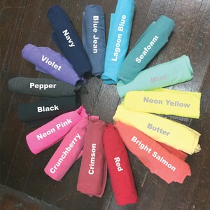 May include: A colour chart of fabric swatches rolled up in a circle. The colours are: Navy, Blue Jean, Lagoon Blue, Seafoam, Mint, Neon Yellow, Butter, Bright Salmon, Red, Crimson, Crunchberry, Neon Pink, Black, Pepper, Violet.