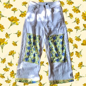 May include: White denim pants with floral patches on the knees. The patches are yellow, green, and blue.