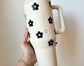 Könnte beinhalten: Eine weiße Reise-Thermoskanne mit einem schwarzen Gänseblümchenmuster und dem Text "HYDRO JUG" an der Seite.
