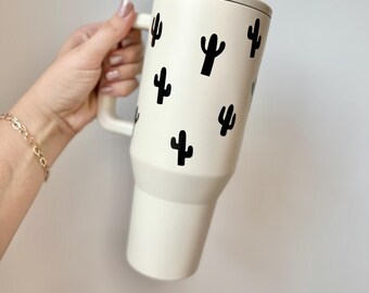 Könnte beinhalten: Weiße Reisebecher mit einem schwarzen Kaktus-Design. Der Becher hat einen Deckel und einen Griff.