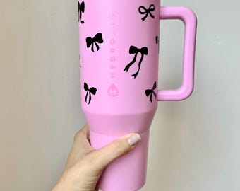 Könnte beinhalten: Rosa HydroJug mit schwarzem Griff und schwarzen Schleifendesigns. Der Text "HYDROJUG" ist auf der Seite der Tasse aufgedruckt.