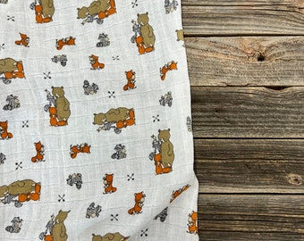 May include: White muslin fabric with a repeating pattern of brown bears and orange foxes. The fabric has a subtle grid pattern.
