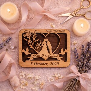May include: Wooden wedding announcement with a heart-shaped cutout featuring a kissing couple silhouette. The text "Save The Date," "Kate & Michael," and "5 October, 2029" are engraved on the wood. The announcement is surrounded by candles, ribbons, and flowers.