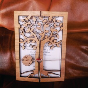 May include: A wooden wedding invitation with a tree design. The invitation is open to reveal the details of the wedding, including the date, time, and location. The invitation is tied with a string and a wooden tag that says "H & J".