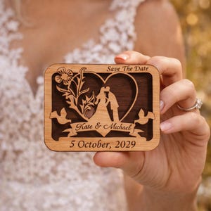 May include: A wooden rectangular wedding announcement with a heart-shaped cutout featuring a couple kissing. The announcement includes the text "Save The Date," the names "Kate & Michael," and the date "5 October, 2029."