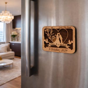 May include: Wooden rectangular magnet with a laser-cut design. The magnet features a heart-shaped silhouette of a couple, floral elements, and the text "Save The Date" and "Kate & Michael 5 October, 2029".