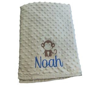 May include: A beige baby blanket with a brown monkey and the name "Noah" embroidered in blue.