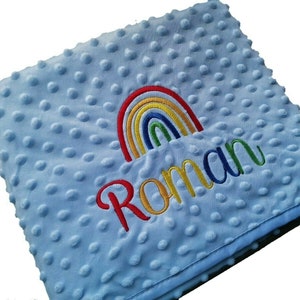 May include: A light blue baby blanket with a rainbow and the name "Roman" embroidered on it.