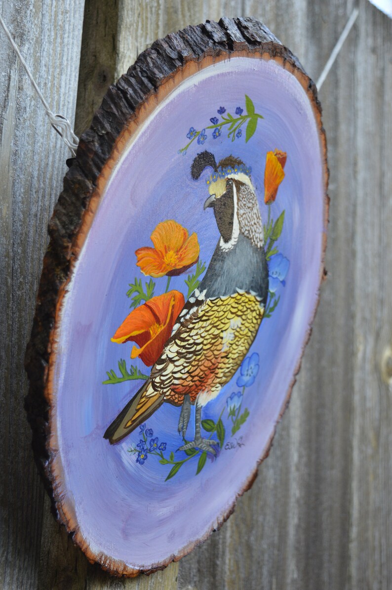May include: A hand-painted wooden slice with a purple background features a colorful California Quail with a crown of blue flowers. The bird is surrounded by orange poppies and blue forget-me-nots.