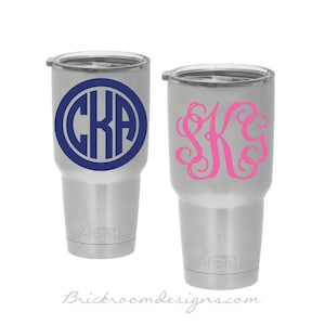 May include: Two stainless steel tumblers with personalized monograms. The tumbler on the left has a navy blue circle with the monogram "CKA" in white. The tumbler on the right has a pink monogram "SK" in a cursive font.