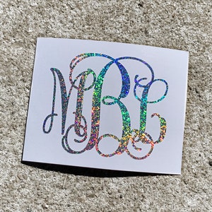 May include: A white background with a silver glitter monogram of the letters "MRE" in a cursive font.