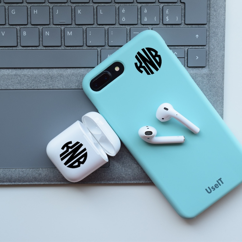 May include: A light blue phone case with a white monogram sticker on the back. The case is on a grey keyboard with white wireless earbuds next to it. The phone case has the text "UselT" printed on the bottom right corner.