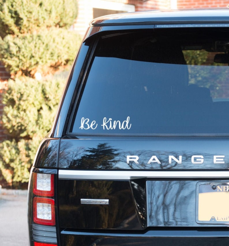 May include: A black car with a white "Be Kind" decal on the back window. The car has a "RANGE" emblem on the back and a license plate.