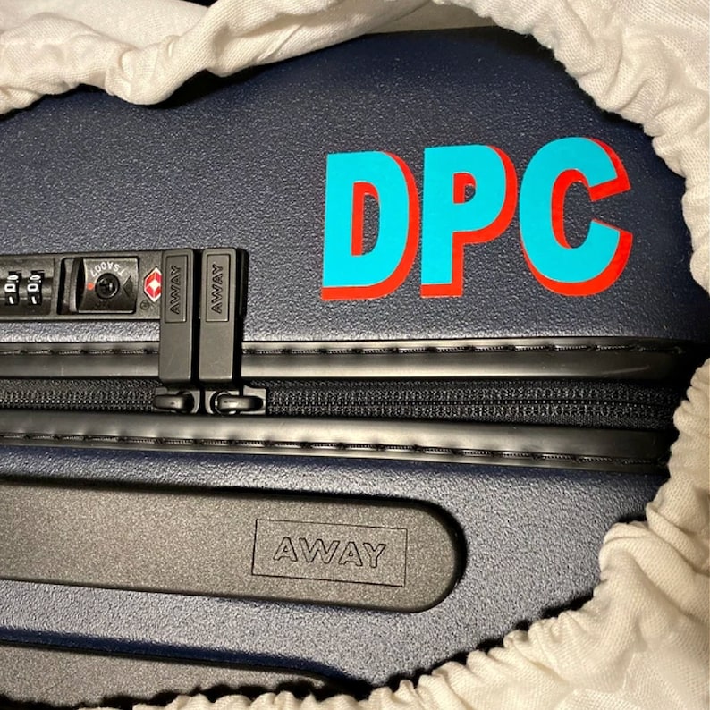 May include: A dark blue suitcase with a black zipper and a black handle. The suitcase has a combination lock and a label that says "AWAY". The suitcase also has a sticker that says "DPC" in blue and red letters.