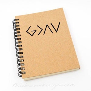 May include: A brown spiral bound notebook with a black graphic of the words "God is greater than" written in a stylized font.