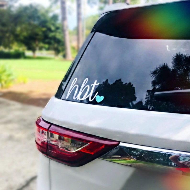 Pode incluir: Carro branco com um cora&ccedil;&atilde;o azul e o texto "hbt" na janela traseira.