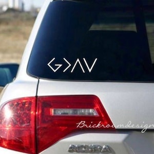 May include: White vinyl decal with the words "God is greater than the highs and lows" represented by geometric shapes. The decal is on the back window of a silver car.