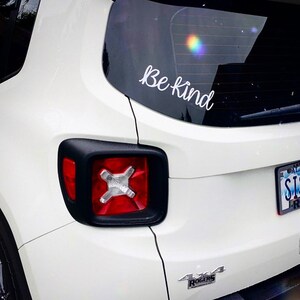 May include: White Jeep with a "Be Kind" sticker on the back window. The car has a black 4x4 emblem on the back bumper.