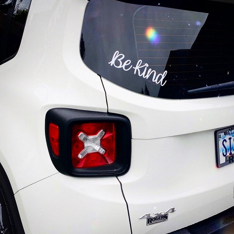 May include: White Jeep with a "Be Kind" sticker on the back window. The car has a black 4x4 emblem on the back bumper.