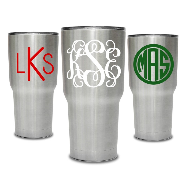 May include: Three stainless steel tumblers with different monogram designs. The first tumbler has the monogram "LKS" in red. The second tumbler has the monogram "KSE" in white. The third tumbler has the monogram "MAS" in green.