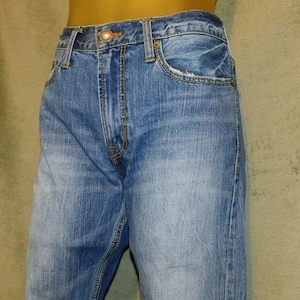 May include: Light blue denim jeans with a classic five-pocket design. The jeans feature a button and zipper closure, belt loops, and a faded wash for a worn look. The jeans are made of a durable denim fabric.