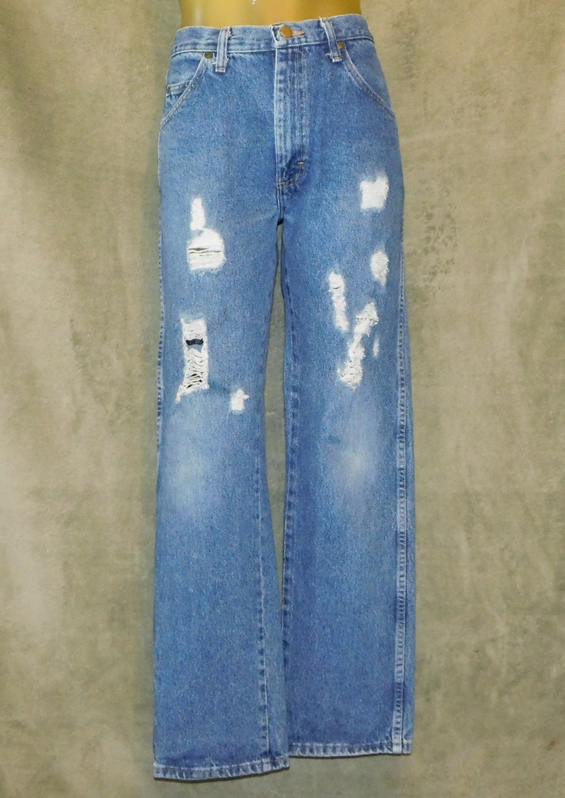 May include: Light blue denim jeans with distressed details. The jeans have a high waist and a wide leg. Several areas of the jeans are ripped and torn, with white patches. The jeans are displayed on a mannequin.