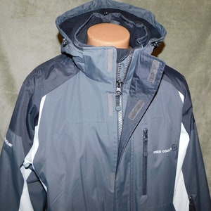 May include: A gray and black winter jacket with a hood. The jacket has a zipper closure and multiple pockets. White accents are on the sides. The brand name "FREE COUNTRY" is printed on the front.