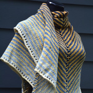 May include: A striped knitted shawl in shades of blue and yellow. The shawl is folded and draped over a mannequin.