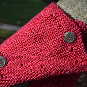 May include: A close-up of a red knitted scarf with two silver buttons. The buttons have a floral design.