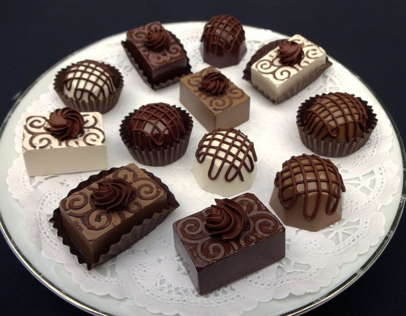 A white plate with a brown and white doily holds an assortment of chocolate fake candies and truffles. The candies are decorated with swirls and lines of chocolate.
