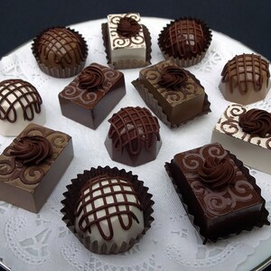 A white plate with a variety of chocolate photo prop candies and truffles. The candies are decorated with swirls, lines, and other designs. Some of the candies are white, while others are brown.