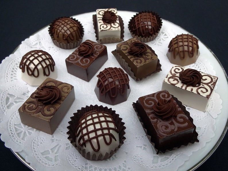 A white plate with a variety of chocolate photo prop candies and truffles. The candies are decorated with swirls, lines, and other designs. Some of the candies are white, while others are brown.