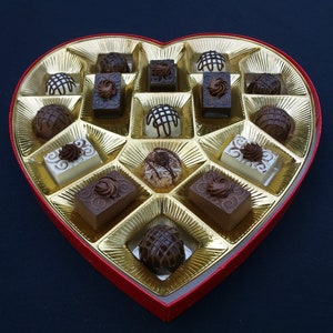A heart-shaped box filled with assorted fake chocolates. The chocolates are arranged in a grid pattern and are a variety of colors and shapes.