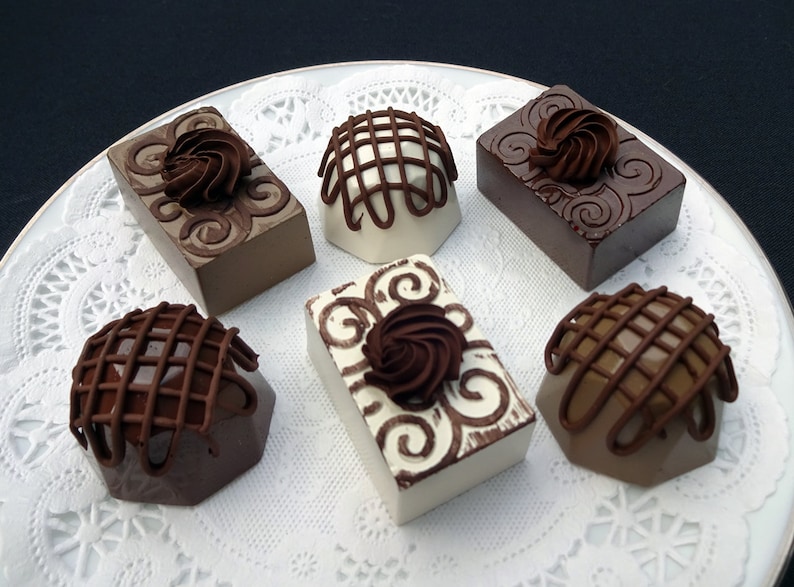 Six assorted chocolate fake truffles on a white lace doily. The truffles are decorated with swirls, lattice patterns, and rosettes.