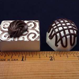 Two fake chocolate candies, one with a swirl design and the other with a lattice design, are shown next to a ruler. The candies are approximately 1 inch in size.